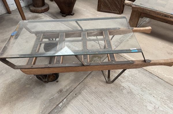 Tablero rectangular de vidrio sobre bastidor de madera con rueda, herrajes y dos mangos; uno continúa fuera de la imagen.