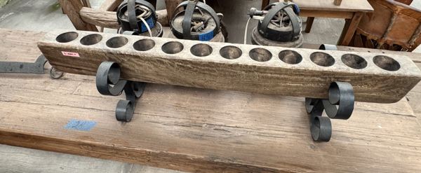 Pieza alargada de madera con una fila de orificios y dos soportes metálicos de extremos curvos, sobre una mesa.