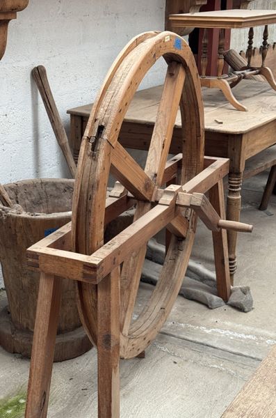 Rueda grande de radios de madera montada en un bastidor con manivela lateral; las patas delanteras salen del encuadre.