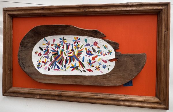 Pieza irregular de madera con motivos multicolores, fondo naranja y marco de madera.