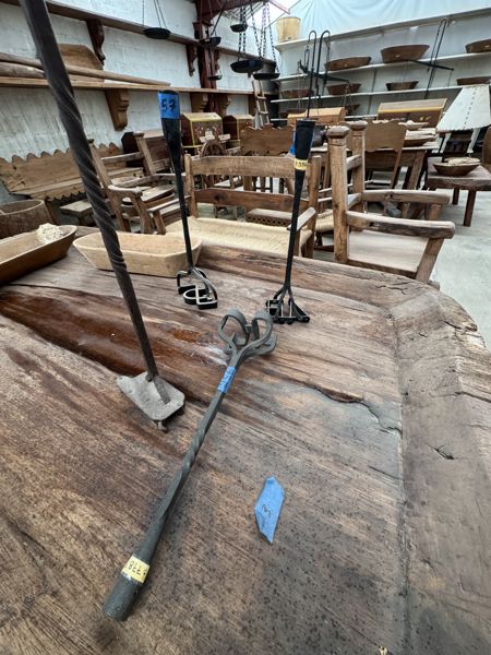 Utensilios metálicos largos, unos verticales y otro diagonal, sobre una superficie de madera de borde grueso, con vetas y grietas visibles.