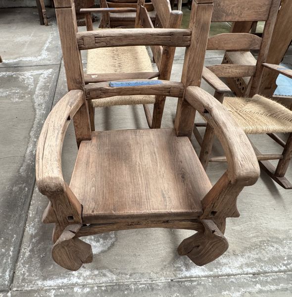 Sillón de madera con asiento sólido, brazos curvos, respaldo de travesaños y elementos inferiores curvos; los postes traseros llegan al borde superior.