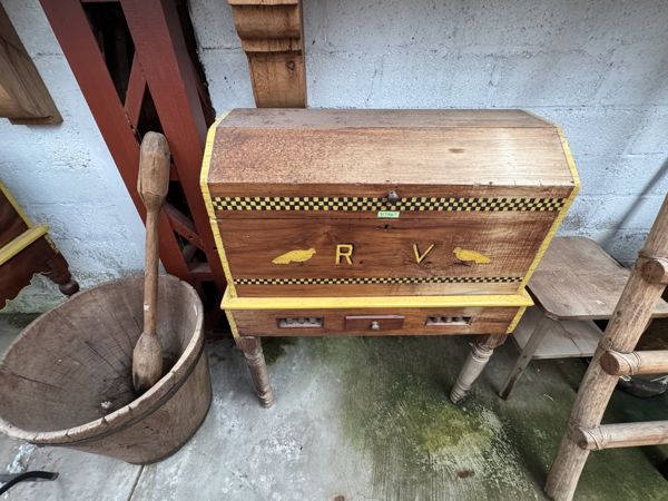 Mueble marrón con bordes amarillos, cenefa geométrica y letras R V; a la izquierda aparece un recipiente de madera.