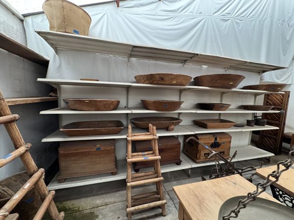 Recipientes redondos y alargados sobre estantes blancos, con dos muebles de madera abajo y una escalera delante.