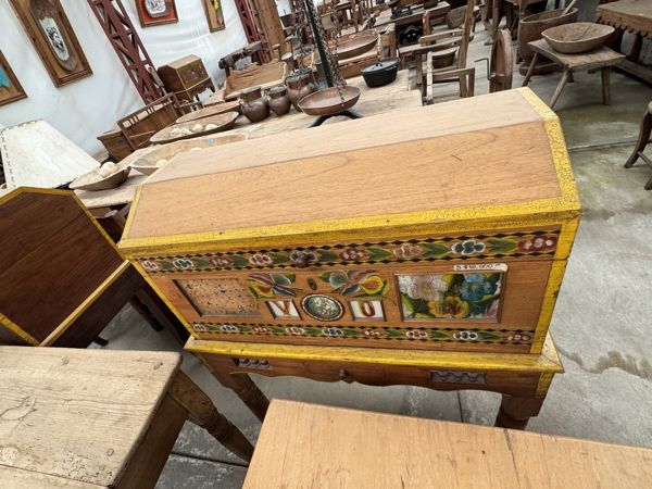 Mueble de madera con bordes amarillos, flores multicolores, cenefas geométricas y motivo ovalado central, sobre una base de faldón recortado.