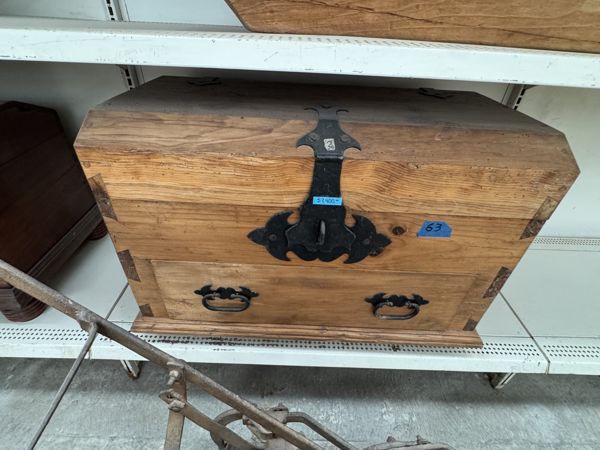 Mueble de madera con veta visible, una larga banda metálica central, placa de contorno ornamental y dos asas ovaladas en el frente inferior.