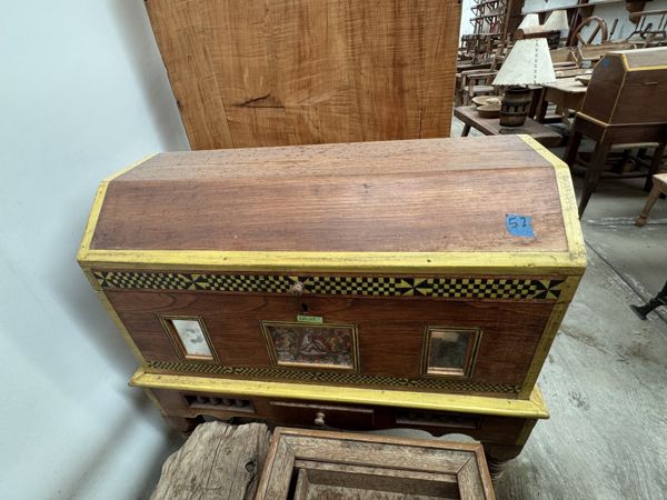 Mueble marrón con bordes amarillos, bandas de cuadros negros y amarillos y tres paneles frontales enmarcados; piezas de madera cubren parte de la base.