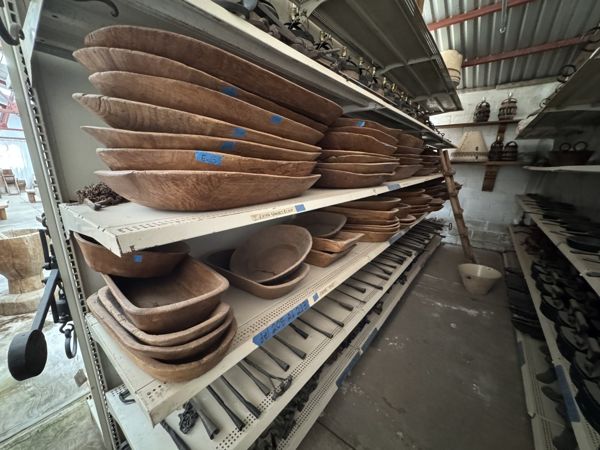 Vista diagonal de estanterías con grandes recipientes de madera superpuestos y cuencos redondos y ovalados en el nivel inferior.