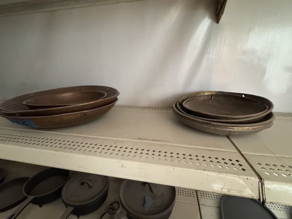 Dos pilas de platos y cuencos poco profundos de madera, con bordes elevados y tonos marrones, sobre una repisa metálica.