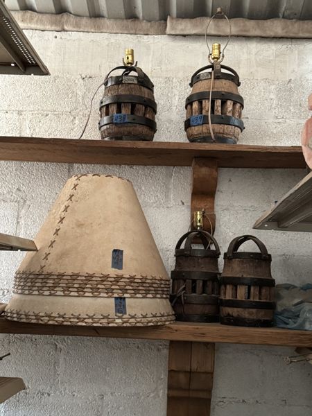Pantallas de lámpara acampanadas de tonos crema y marrón, con cordones cruzados en bordes y costuras, junto a bases de madera con bandas metálicas.