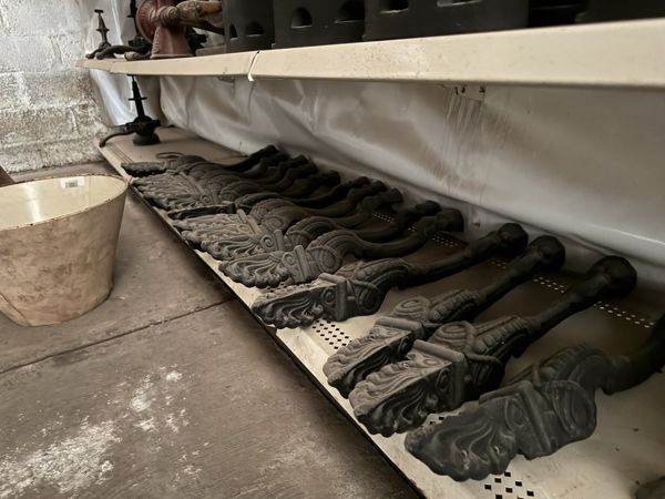 Piezas metálicas alargadas y curvas en una repisa baja, con extremos anchos decorados con relieves de volutas y hojas.
