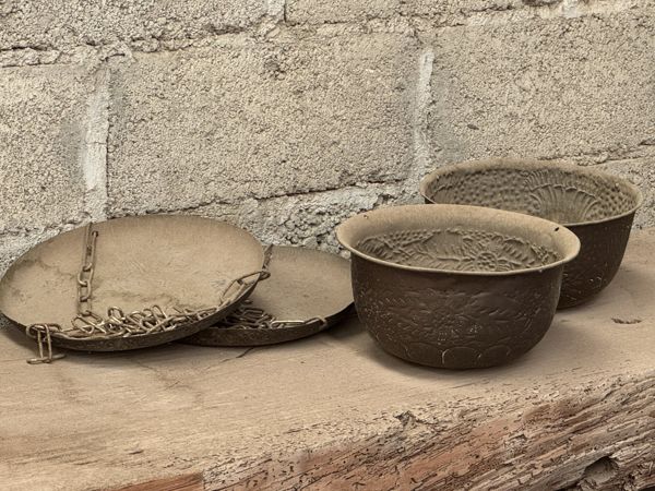 Platillos metálicos poco profundos con cadenas y dos cuencos de superficies decoradas sobre una repisa de madera.