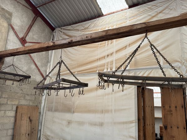 Varias estructuras metálicas con ganchos orientados hacia abajo cuelgan mediante cadenas de una viga de madera.