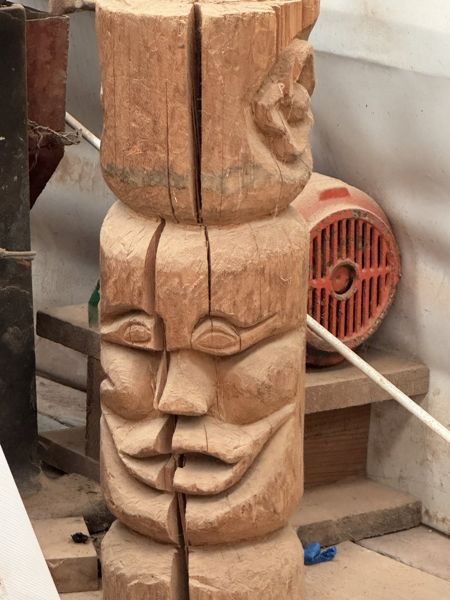 Detalle de una talla vertical de madera con ojos, nariz y boca en relieve y una profunda grieta longitudinal; los extremos quedan fuera del encuadre.