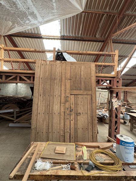 Panel alto de tablas verticales con un detalle rectangular en el lado derecho, bajo una plataforma de madera y detrás de una estructura baja con objetos.