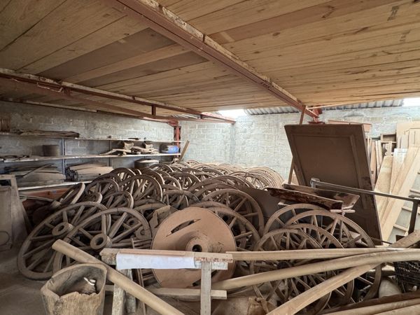 Ruedas de radios, aros, cubos, ejes y bastidores de madera apilados bajo una plataforma, junto a un disco circular con abertura central.