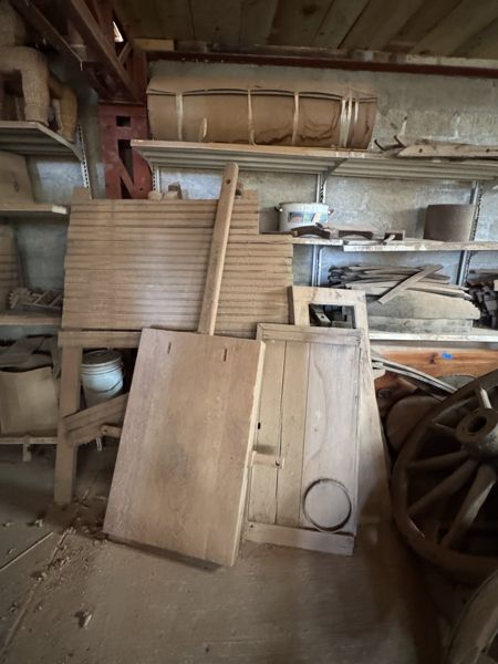 Persiana alta de lamas y paneles de madera apoyados frente a estanterías; el panel derecho presenta un detalle circular y una rueda asoma en el borde.