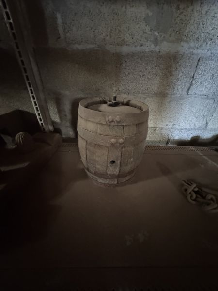 Recipiente de madera formado por duelas verticales y tres bandas, con panel superior hundido y pequeño remate en forma de T.