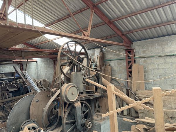 Estructura mecánica alta con gran rueda superior de radios, ruedas menores y una pieza curva lateral, detrás de cuerdas y postes.