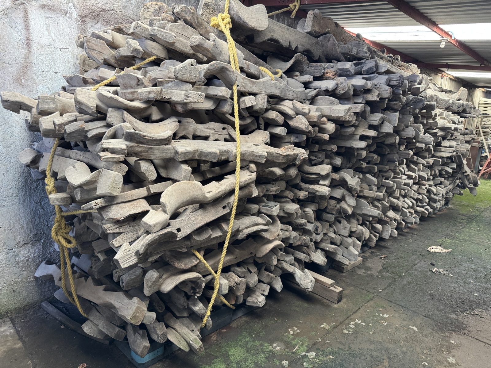 Pila de vigas menores y madera recuperada bajo techo.