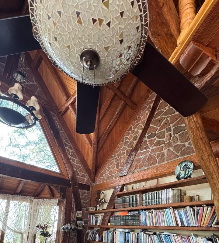 Biblioteca de doble altura con entramado de madera y muros de piedra en Finca La Cima