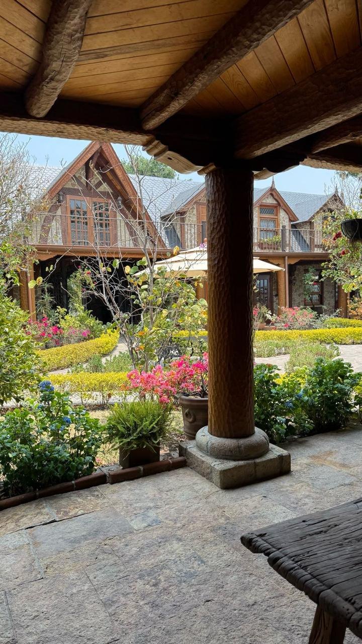 Patio cubierto con vigas talladas y vista al jardín interior de Finca La Cima